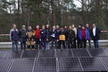 Gruppenfoto vom PV-Bau am 3.12.2024 auf dem Gebäude des Lehrstuhls für Laserphysik. Im Vordergrund sind installierte PV-Module zu sehen. Dahinter steht die Gruppe der Beteiligten.