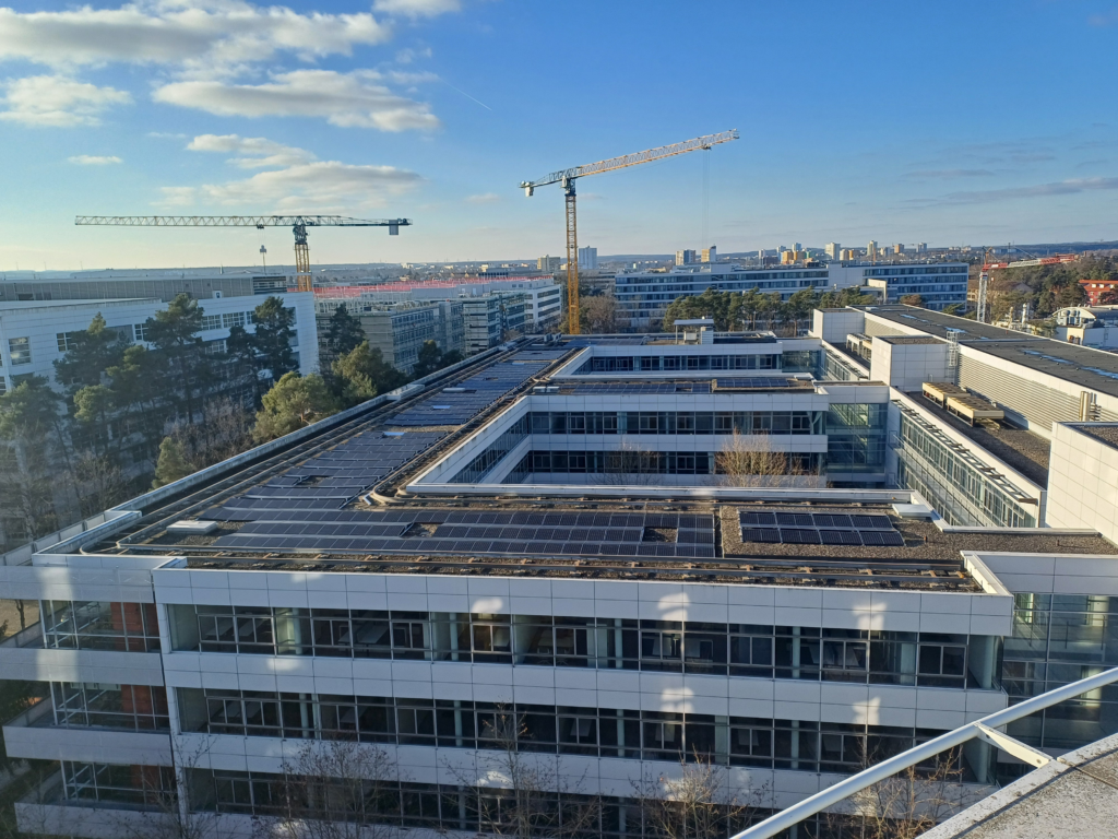 Fotoaufnahme von einem Flachdach mit einer PV-Anlage. Im Hintergrund sieht man zwei Kräne und den Himmel.