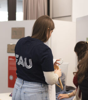 Das Bild zeigt eine Person mit FAU-Tshirt, die gerade Kleidung auf einen Bügel hängt.