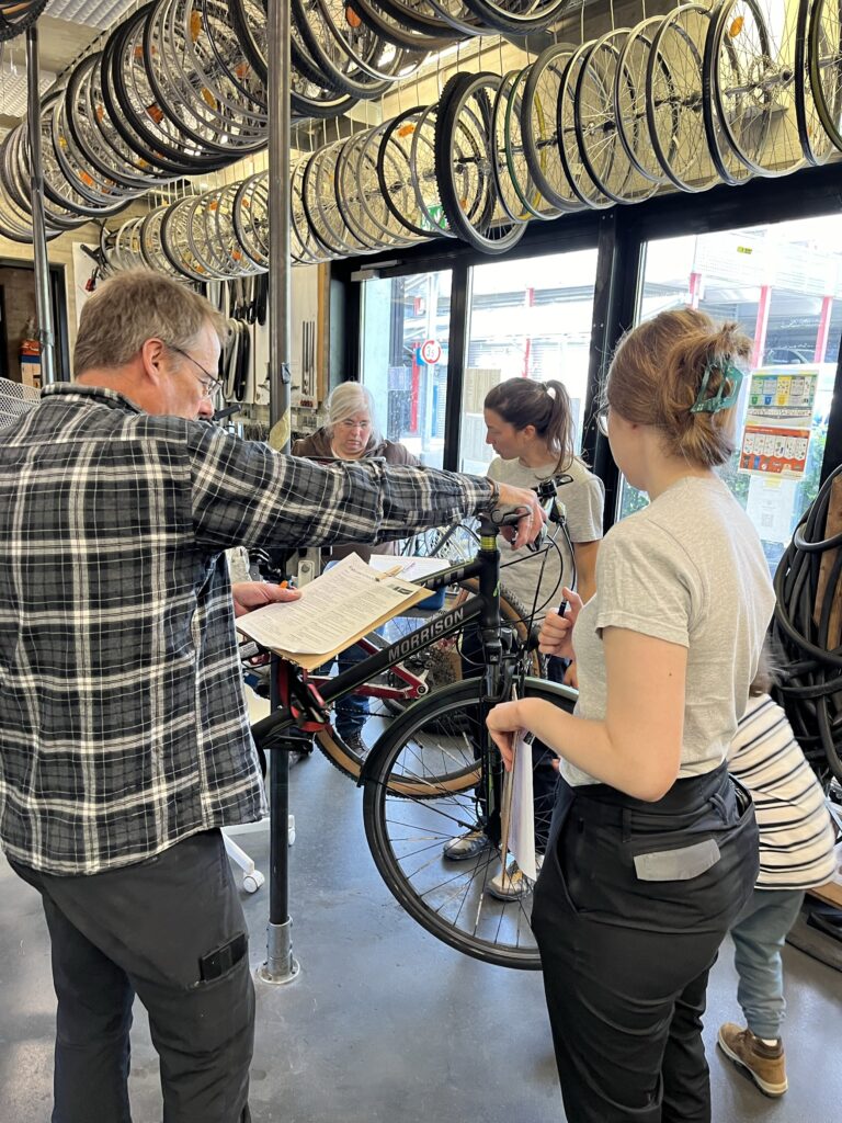 Zu sehen sind mehrere Personen, die gerade Reparaturschritte an einem Fahrrad erklärt bekommen.