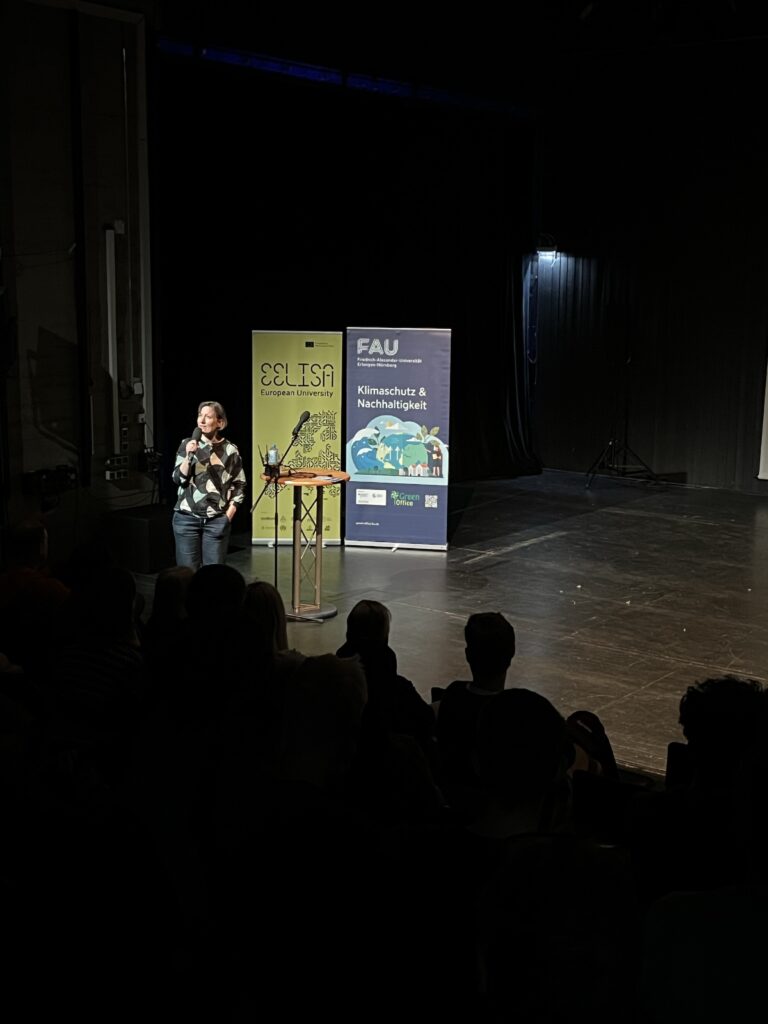 Zu sehen sind Roll-Ups von EELISA und dem Green Office, ein Publikum und eine Person auf der Bühne.