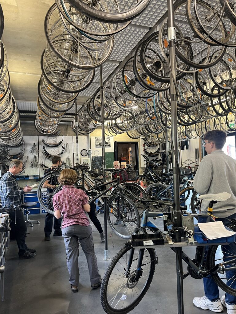 Zu sehen sind mehrere Personen, die gerade Reparaturschritte an einem Fahrrad erklärt bekommen.