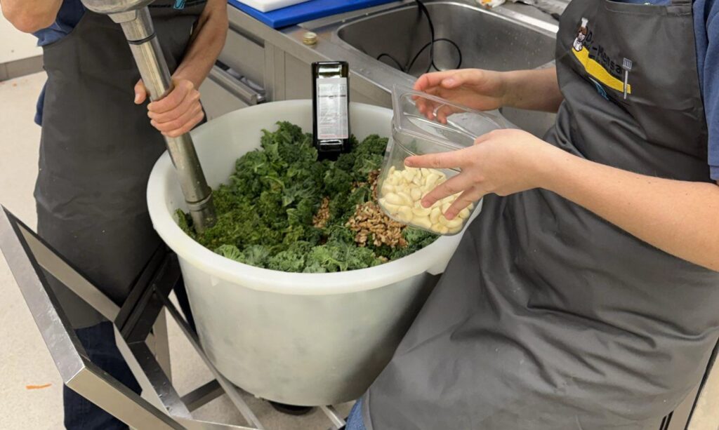 Auf dem Foto ist ein großer Eimer, gefüllt mit Gemüse zu sehen, was gerade mit einem großen Pürierstab püriert wird.