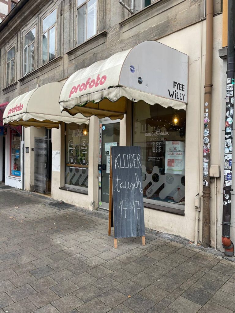 Auf dem Bild ist eine beschriftete Tafel auf dem Gehweg vor dem Umsonstladen zu sehen. AUf der Tafel steht "Kleidertausch, 14-17 Uhr".