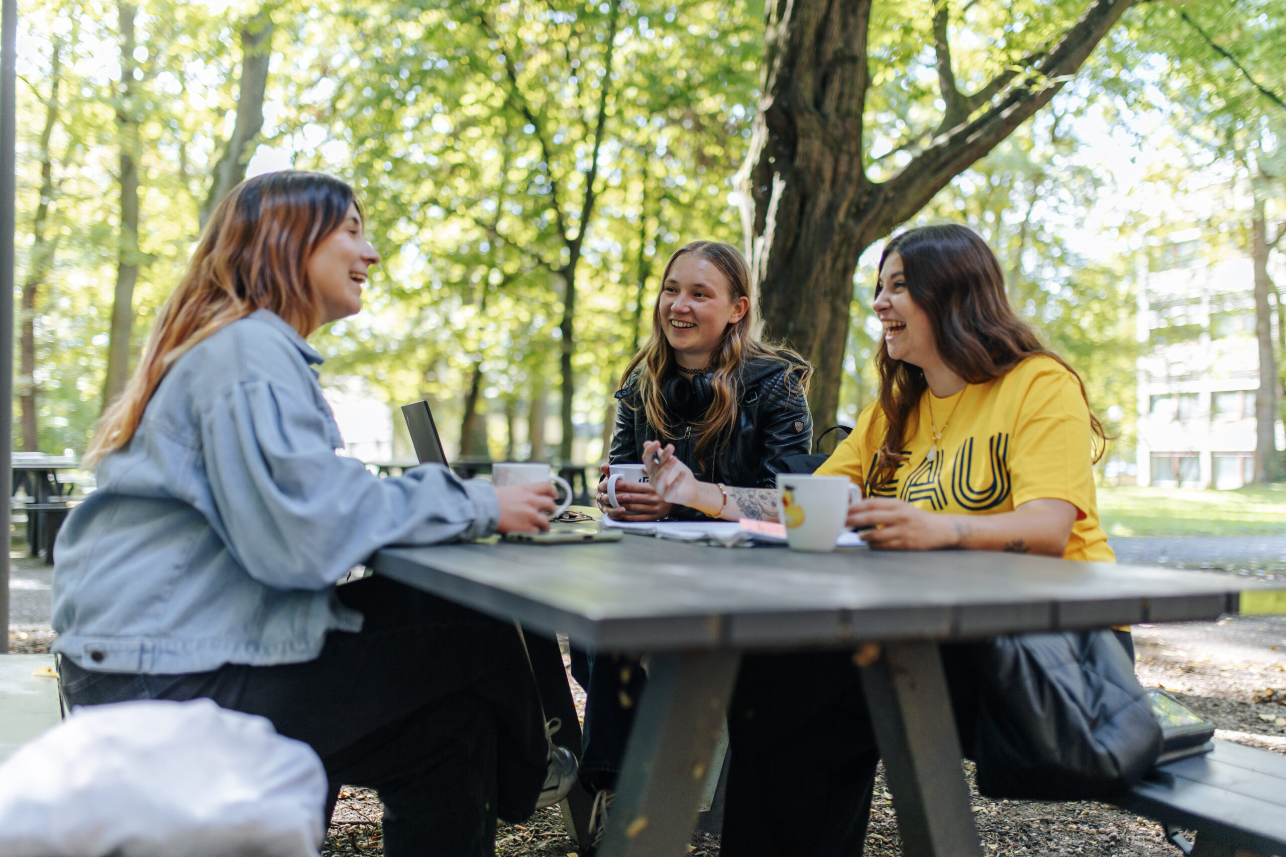 Drei Studentinnen sitzen im Freien an einem Tisch und tauschen sich fröhlich aus